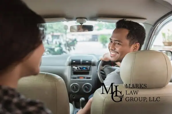 Smiling driver turning to speak with a passenger seated in the back of a car