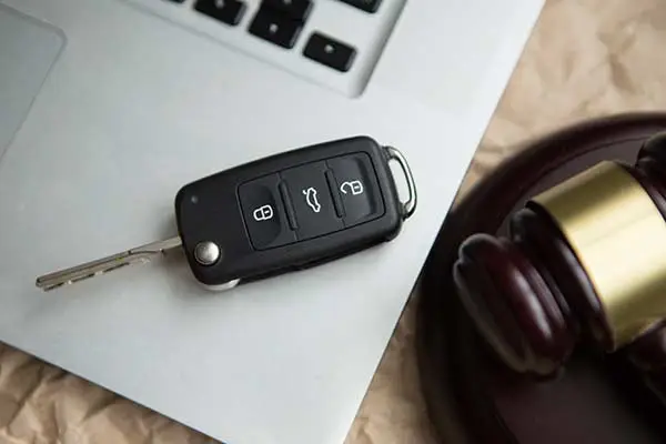 A car key fob lying on a laptop next to a wooden gavel